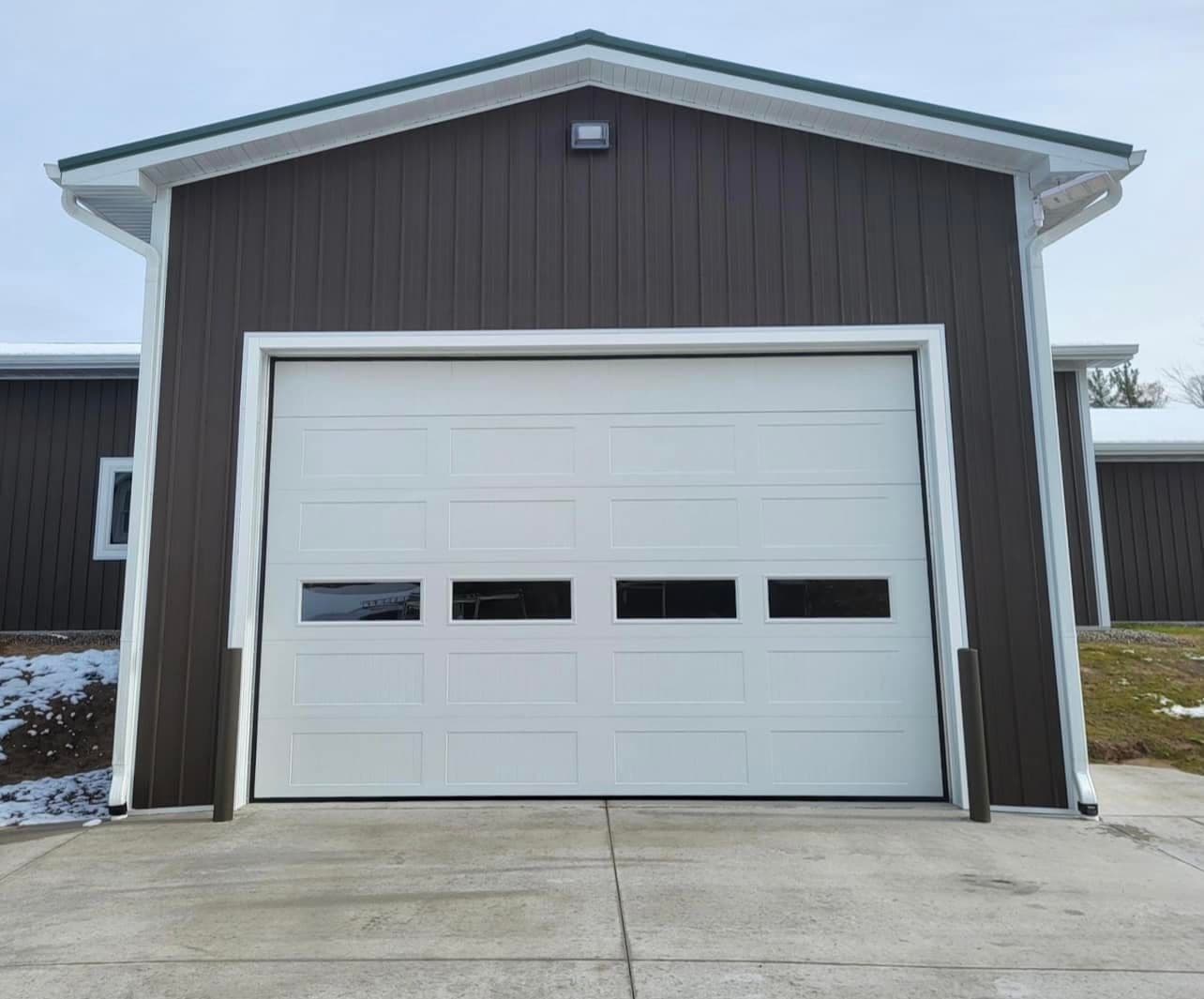 White insulated garage door with windows on a dark steel pole building